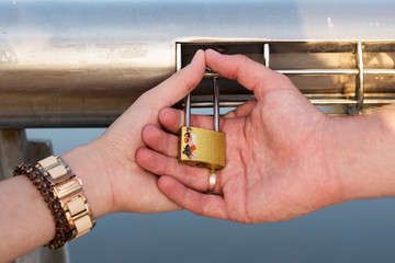 The hands hold the lock buttoned on the railing of the bridge
