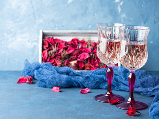 Two stemmed champagne glasses on blue textured background with pink dried flowers. Valentine's day wedding romantic date invitation