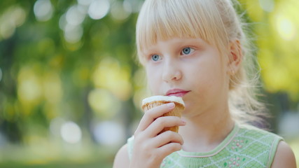 Thoughtful girl 6 years old is eating ice cream in the park. Holiday in summer and vacations