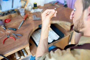Fototapeta na wymiar Portrait of jeweler looking at ring through magnifying glass in workshop