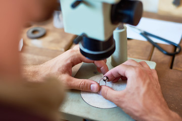 Closeup portrait of unrecognizable jeweler inspecting  ring using microscope on workshop table