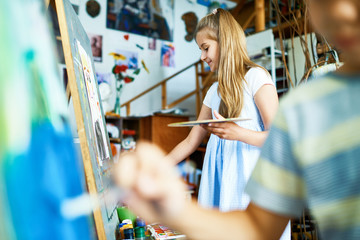 Fototapeta premium Cheerful pretty girl with palette in hand sharpening her drawing skills while having class at modern art studio