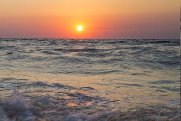 Fototapeta na wymiar Il sole che tramonta nel mare è sempre una bella chiusura per una giornata di vacanza. Le tonalità calde donate dal sole si scontrano con il blu delle acque agitate del mare.