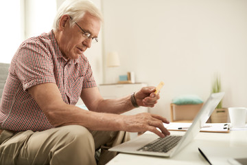 Side view portrait of senior man online shopping via laptop inputting credit card details for...