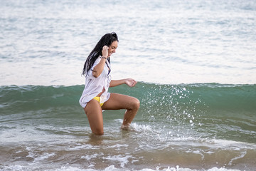 Chica joven con camisa blanca jugando con las olas en el mar al atardecer.