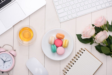 White desk with colorful macaroons, keyboard and open notebook.