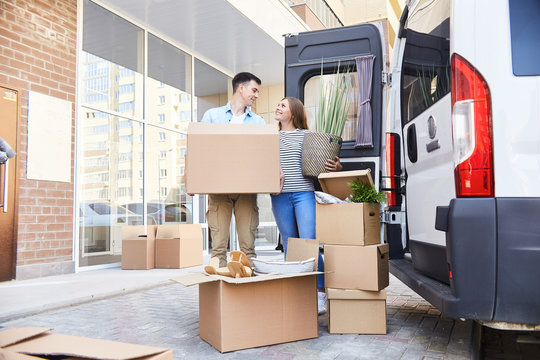 Portrait of happy young couple posing with cardboard boxes standing next to moving van outdoors
