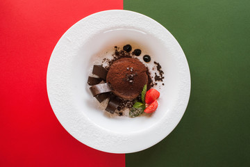 Chocolate fondant on colorful background of red and green. Delicious dessert with decoration from strawberry and mint serving in restaurant, top view with free space