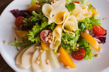 Lettuce salad with cheese and fruits on plate. Fresh vegetables decorated pine nuts, avocado, pearch and pear, serving in restaurant, close up picture