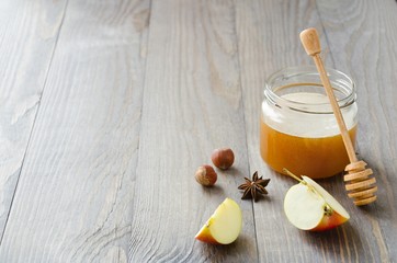 Fototapeta na wymiar Jar of honey with honey stick, slices of apple, hazelnuts and anise