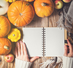 Womans hands on the notebook and pumpkins on wood background