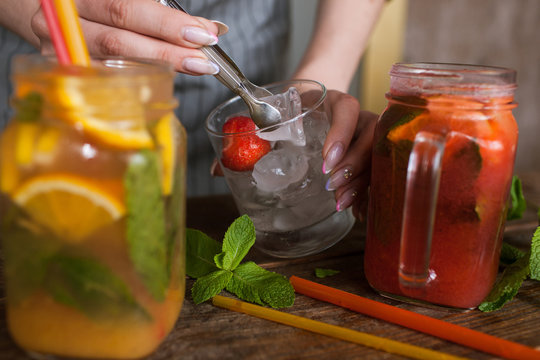 Waiter puts piece of ice into fruit cocktails. Fresh citrus and strawberry cold drink with mint on wooden table, concept of refreshment and satisfying thirst in summer, close up picture