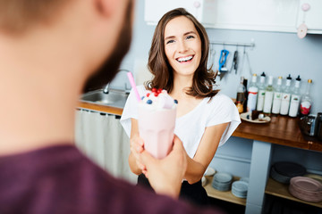 smiling woman giving milkshake to customer in stylish modern cafe