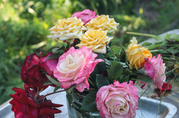 a bouquet of yellow pink and red roses lies on an old metal tray