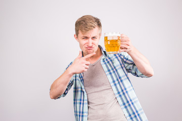Cheerful young man holding a beer mug full of beer and smiling on white background