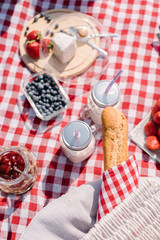 Picnic in the nature with croissants, peaches, strawberries, blueberries, grapes, baguette, cheese and glass bottles of milk