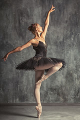 Young beautiful woman prima theater in a black festive pack, white pantyhose, white pointe shoes beautifully dancing russian ballet in a black dance studio