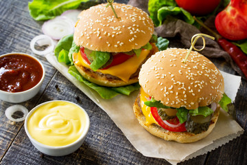 A double burger with a meat cutlet and vegetables is served with cheese sauce and ketchup. Delicious fresh homemade double cheeseburger on a wooden kitchen table. Street food, fast food.