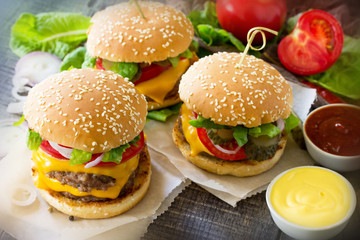 A double burger with a meat cutlet and vegetables is served with cheese sauce and ketchup. Delicious fresh homemade double cheeseburger on a wooden kitchen table. Street food, fast food.