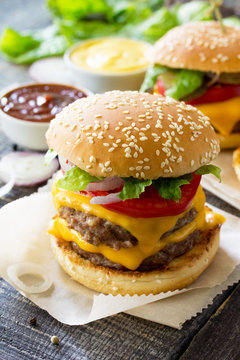 Delicious fresh homemade double cheeseburger on a wooden kitchen table. Double burger with meat cutlet and vegetables. Street food, fast food.