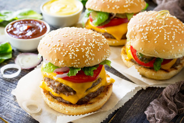 Delicious fresh homemade double cheeseburger on a wooden kitchen table. Double burger with meat cutlet and vegetables. Street food, fast food.