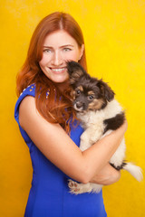 Fototapeta na wymiar beautiful redhaired young woman standing with little cute dog puppy on yellow studio background