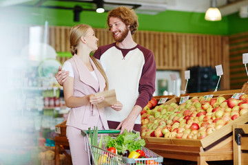 Affectionate couple with shopping list buying products in hypermarket