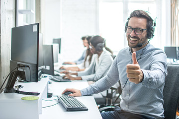 Cheerful male customer service operator showing thumbs up in office.