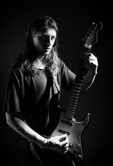 Dramatic studio portrait: handsome long-haired young man (rock musician) playing the electric guitar. Black and white