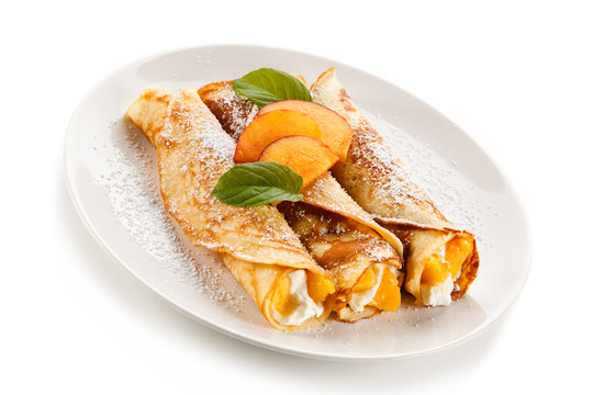 Crepes with peaches and cream on white background 