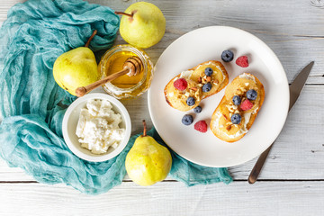 Crostini with ricotta cheese, fried pear, nuts and honey, decorated with raspberries and blueberries