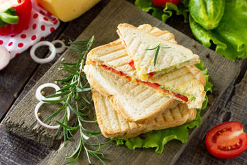Fototapeta na wymiar Pressed and toasted double sandwich with fresh vegetables and cheese, served with lettuce leaves on a cutting board.