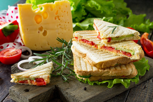 Pressed and toasted double sandwich with fresh vegetables and cheese, served with lettuce leaves on a cutting board.