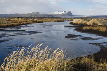 Autumn landscape in Iceland with a river, black sand and dry grass in foreground