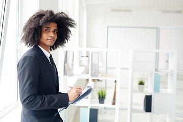 Young financier making notes in document in office