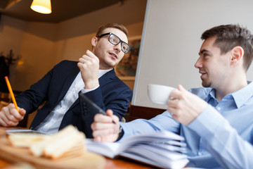 Two confident men having discussion of new working strategies by cup of tea in cafe