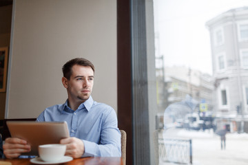 Businessman with touchpad contemplating and looking through window in cafe