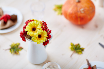 Fototapeta na wymiar Yellow flowers and ripe ashberries in porcelain vase on festive table