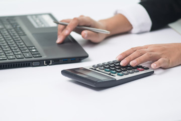 A business woman analyzing investment charts at his workplace and using his laptop and touch calculator.