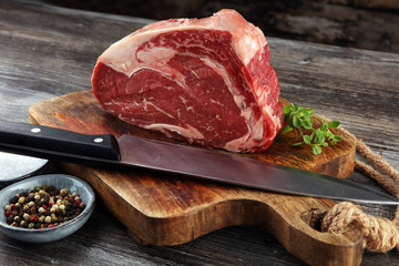 Raw fresh meat Ribeye Steak, seasoning and meat fork on dark background