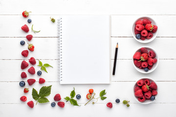 Naklejka na ściany i meble Notebook mock up, pencil and fresh berries on white wooden background . Top view, flat lay.