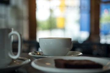 Two white cups of coffee and a piece of brownie cake in a plate on wooden table in vintage cafe