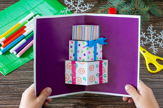 A child holds a birthday card with Christmas presents. Made by own hands. Children's art project, craft for children. Craft for kids.