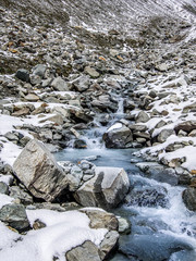 Beautiful view of one mountain river with small waterfalls and snow around. Summer in Valle d'Aosta, Italy, Europe.