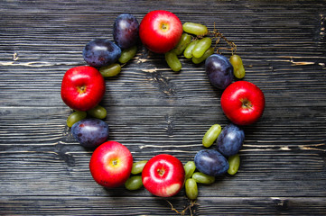 Apples, plums and grapes on a black wooden background