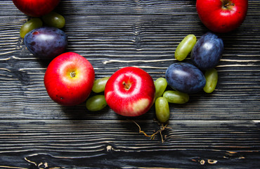 Apples, plums and grapes on a black wooden background