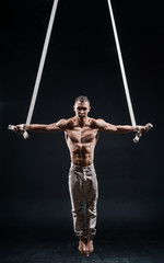 Fototapeta na wymiar circus artist on the aerial straps with Strong muscles on black background
