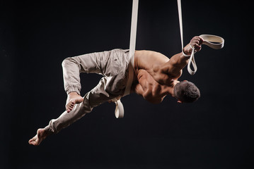 circus artist on the aerial straps with Strong muscles on black background