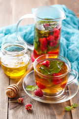 Glass cup of hot tea with raspberries, mint and honey