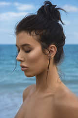 Close-up portrait of a young beautiful well-groomed girl in profile on a blue sky and sea background. Bright lighting - sunlight. Bright colors. Smooth, shiny, well-groomed skin, tan. Advertising.